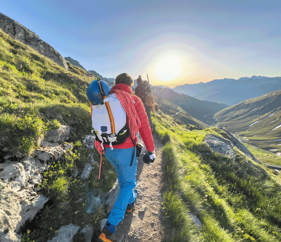 Hiker with a backpack and climbing gear walking along a mountain trail at sunrise, symbolizing adventure, resilience, and the journey ahead